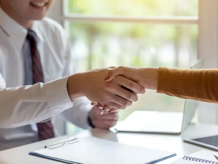 Close-up of two people shaking hands across an office desk, symbolizing partnership and client trust